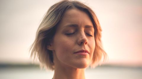 Eine Frau hält sich mit geschlossenen Augen die Hand aufs Herz.