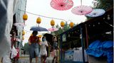 Peking, China. Anwohner suchen Schutz unter ihren Regenschirmen, während sie an einem regnerischen Tag an geschlossenen Verkaufsständen vorbeigehen.