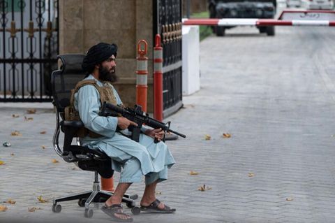 Taliban sitzt mit Maschinengewehr auf Bürostuhl