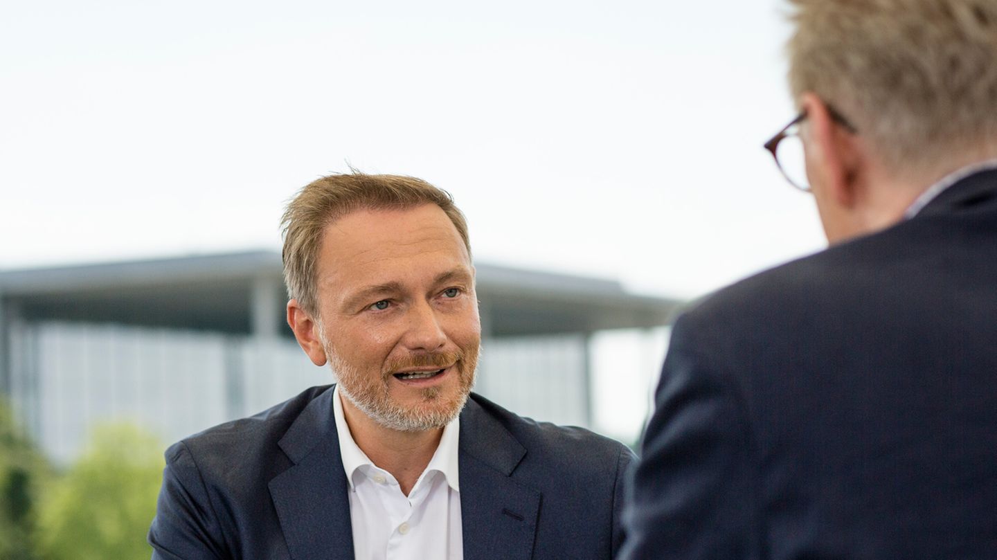 Ein älterer weißer Mann in blauem Anzug sitzt an einen hellgrauen Pult auf einer Wiese vor dem Bundestag