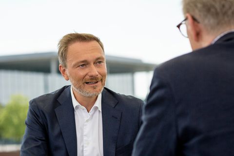 Ein älterer weißer Mann in blauem Anzug sitzt an einen hellgrauen Pult auf einer Wiese vor dem Bundestag