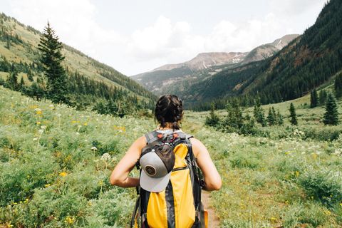 Eine Frau steht mit Wanderrucksack vor einer grünen Berglandschaft.
