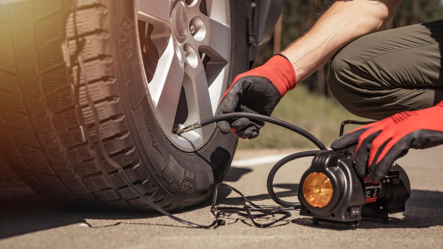 Reifenpannensets im Vergleich: Mann füllt mit mobilem Kompressor Luft in einen Autoreifen.
