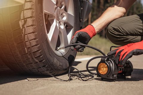 Reifenpannensets im Vergleich: Mann füllt mit mobilem Kompressor Luft in einen Autoreifen.