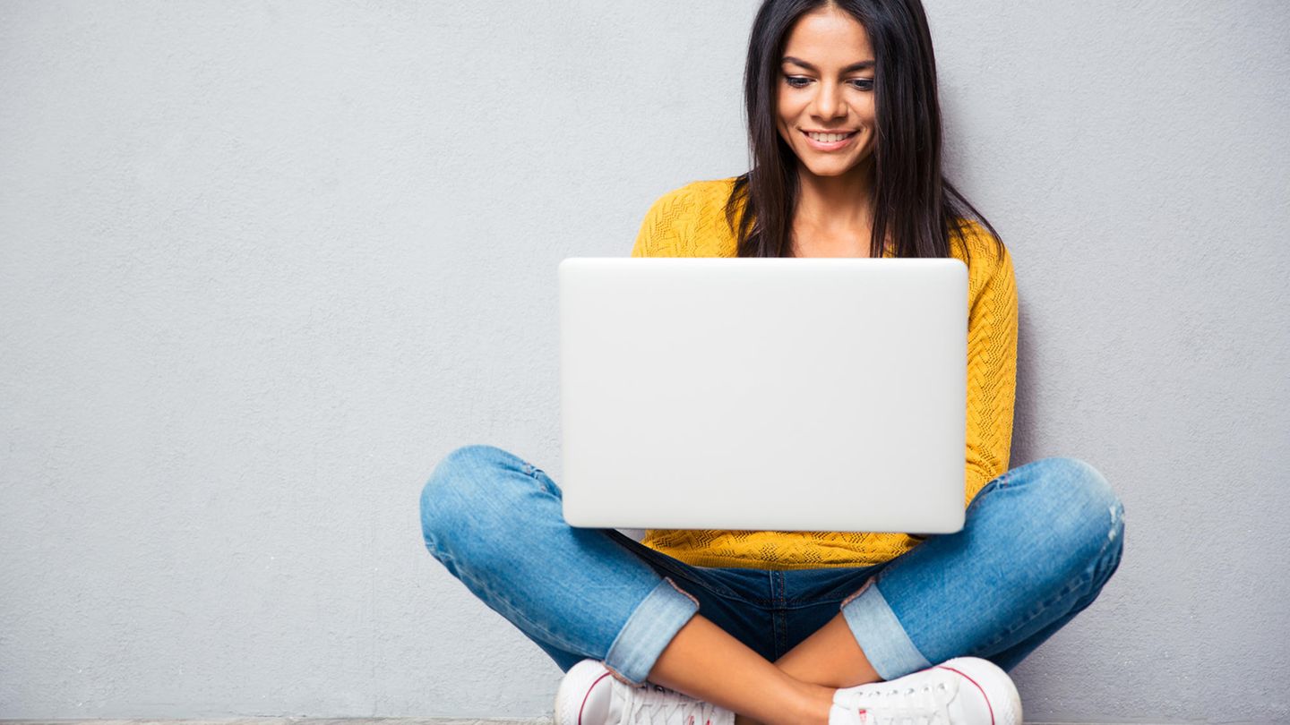 Eine Frau sitzt mit einem Laptop bis 300 Euro auf dem Schoß im Schneidersitz.