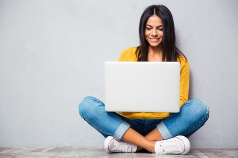 Eine Frau sitzt mit einem Laptop bis 300 Euro auf dem Schoß im Schneidersitz.