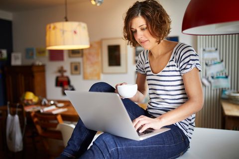 Portrait of mature woman sitting on kitchen table using laptop
