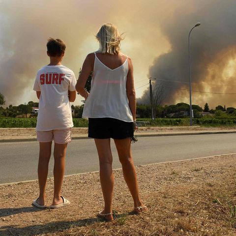 18. August 2021, Südfrankreich: Touristen beobachten, wie Rauch den Himmel verdunkelt, der von Waldbränden ausgeht