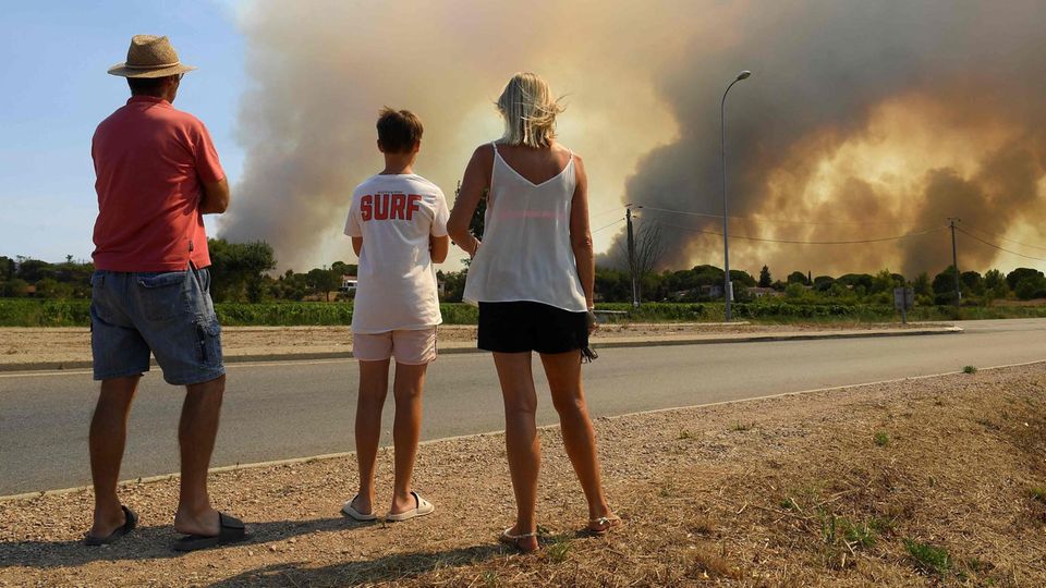 18. August 2021, Südfrankreich: Touristen beobachten, wie Rauch den Himmel verdunkelt, der von Waldbränden ausgeht