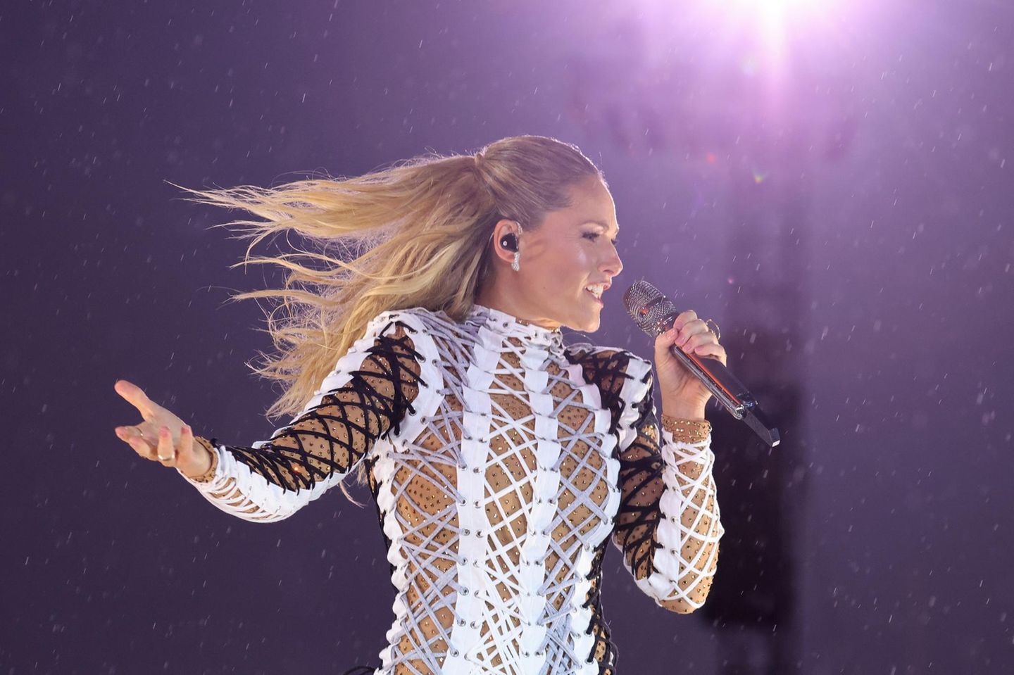 Helene Fischer singt mit wehendem Haar in ein Mikro, während im Hintergrund Regentropfen glänzen
