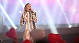 Während Helene Fischer auf der Bühne singt, halten Fans rote Herz-Luftballons hoch