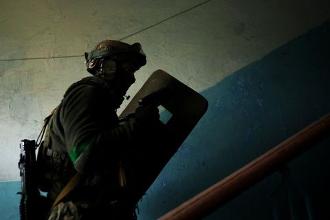Ein Mann mit Uniform, Helm und Schutzschild läuft in einem weiß-blauen Treppenhaus treppauf