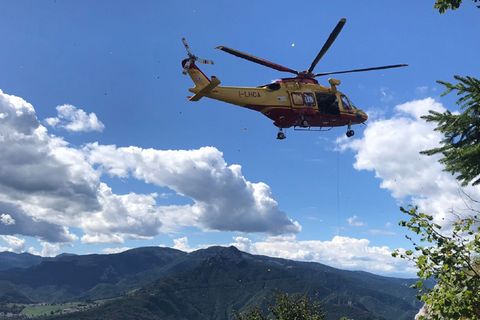 Ein grüner Hubschrauber fliegt über einem Berghang mit Tannen