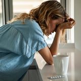 Frau beugt sich über den Tisch, weil sie Kopfschmerzen hat