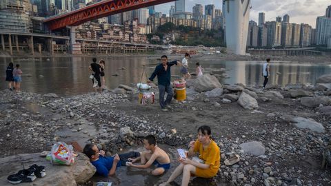 Menschen sitzen in einem flachen Wasserbecken im Flussbett des Flusses Jialing