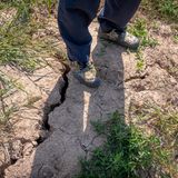 Ein Bauer steht auf einem von der Hitze aufgerissenen Boden