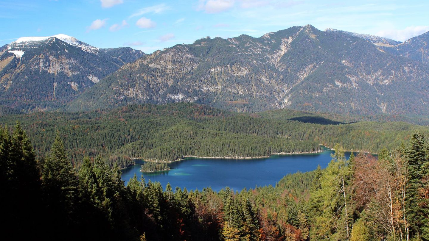 Der Bayerische Wald mit einem Bergsee und den Alpen im Hintergrund.
