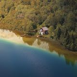 Ein kleines Häuschen steht am Waldrand direkt an einem Seeufer.