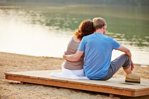 Ein Mann und eine Frau sitzen Arm in Arm auf einem Steg (Symbolbild)