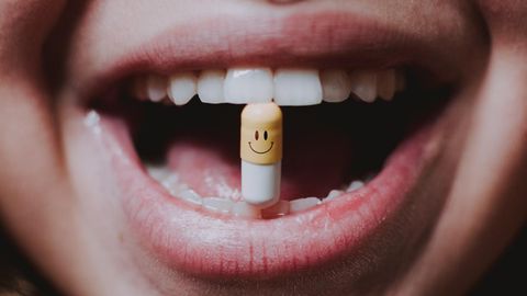 Eine Frau hält eine Kapsel mit einem Smiley darauf zwischen ihren Zähnen.
