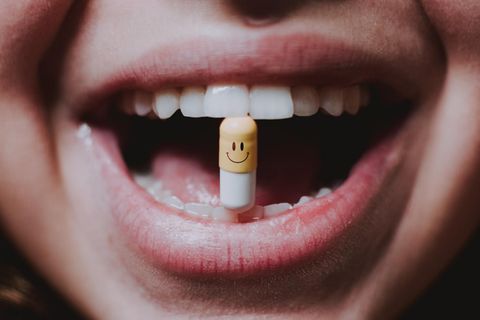 Eine Frau hält eine Kapsel mit einem Smiley darauf zwischen ihren Zähnen.