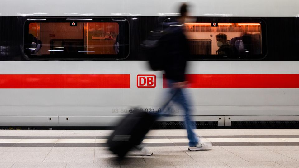 Mann mit Koffer geht an einem ICE vorbei