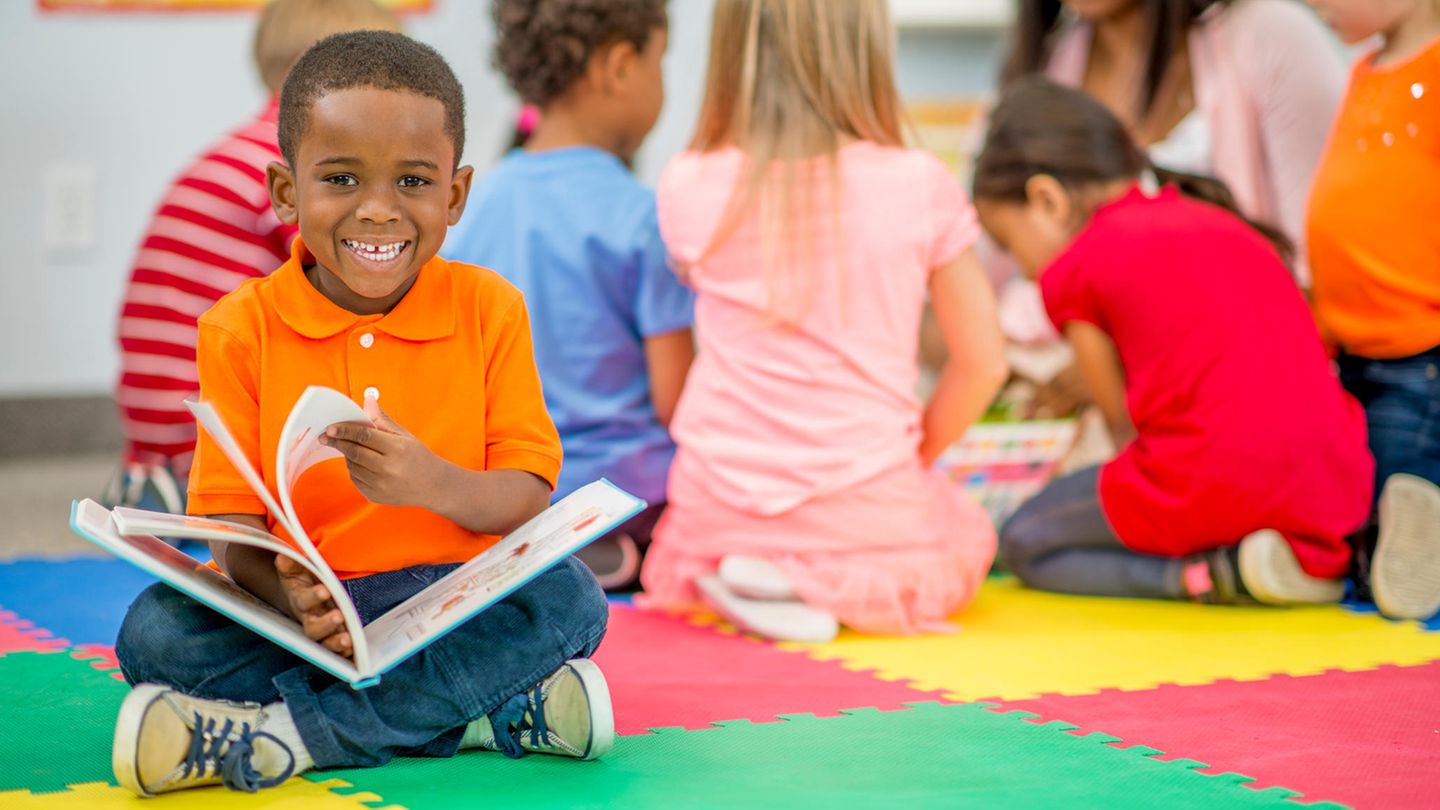 Kleiner Junge schaut in ein Bilderbuch im Kindergarten