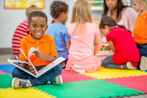 Kleiner Junge schaut in ein Bilderbuch im Kindergarten