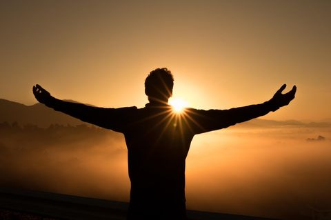 Ein Mann steht mit ausgebreiteten Armen vor einem Sonnenuntergang.
