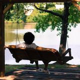 Ein Mann sitzt in einer Hollywoodschaukel und blickt auf einen See.