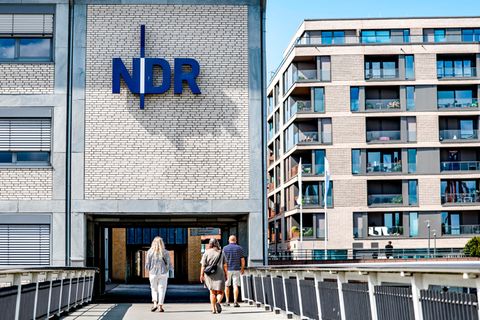 Schleswig-Holstein, Kiel: Passanten gehen vor der Einfahrt zum Landesfunkhaus Schleswig-Holstein des NDR entlang