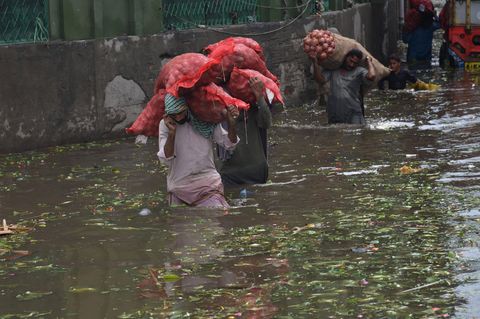 Menschen aus Pakistan waten durch überflutete Straße