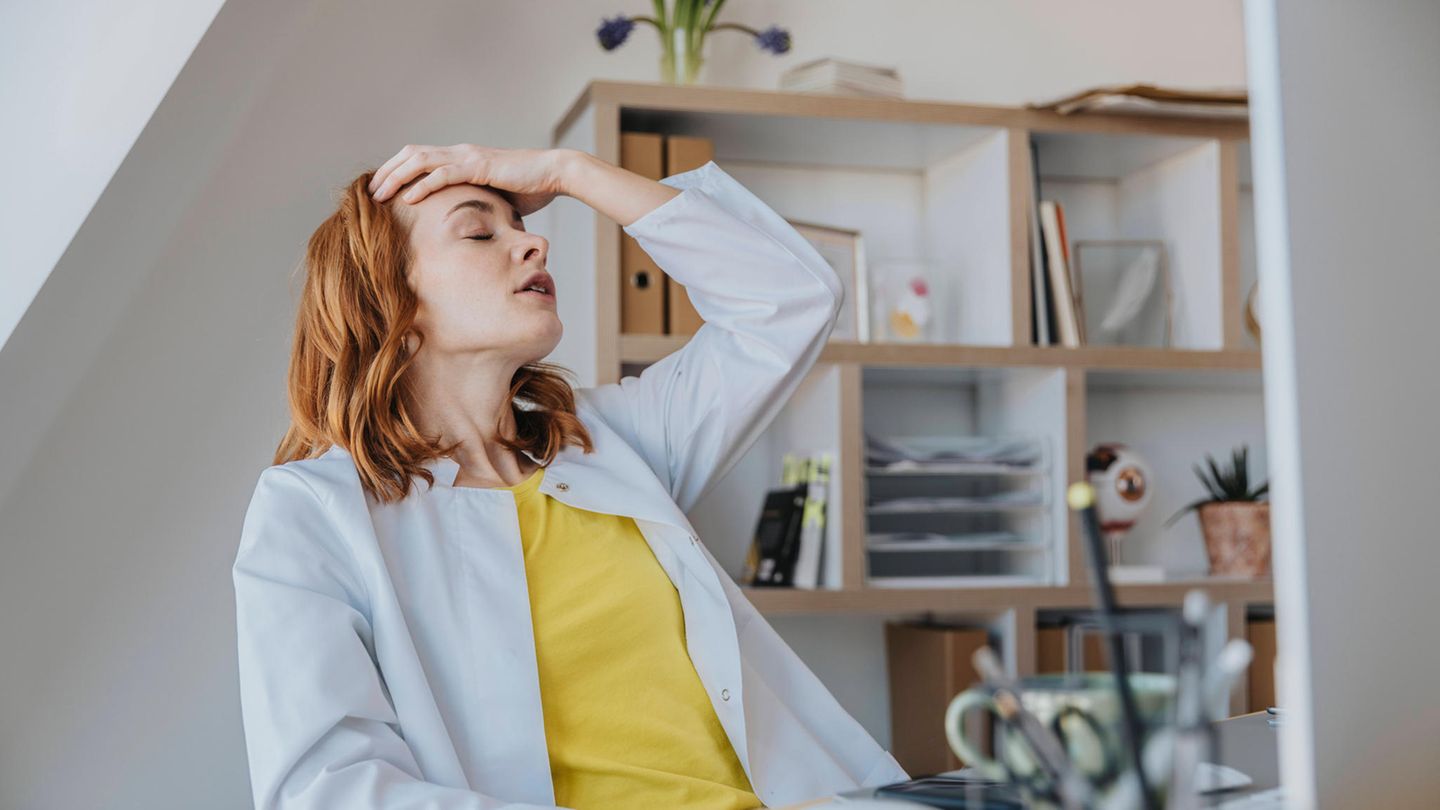 Eine Frau fasst sich im Büro erschöpft an den Kopf.