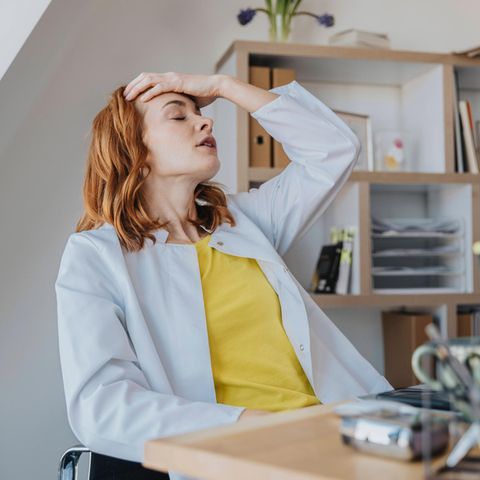 Eine Frau fasst sich im Büro erschöpft an den Kopf.