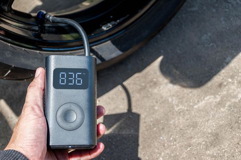 Die Hand, die einen tragbaren Inflator hält, pumpt einen Motorradreifen auf
