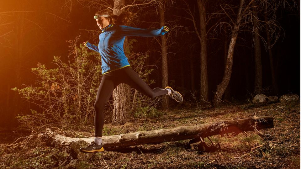Joggen im Dunkeln: Frau beim Trailrunning im Wald mit Stirnlampe