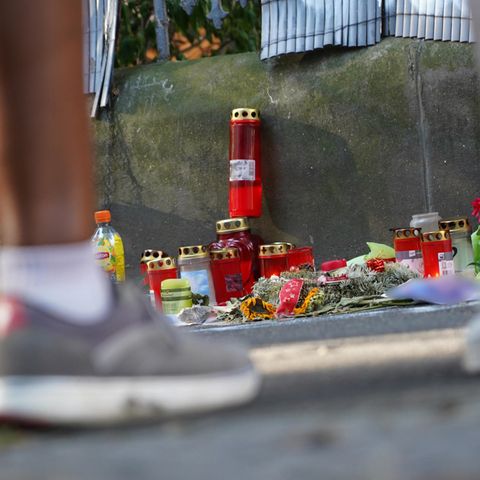 Menschen stehen vor einem Zaun, an dem mit Kerzen und Blumen eines von der Polizei erschossenen Jugendlichen gedacht wird 