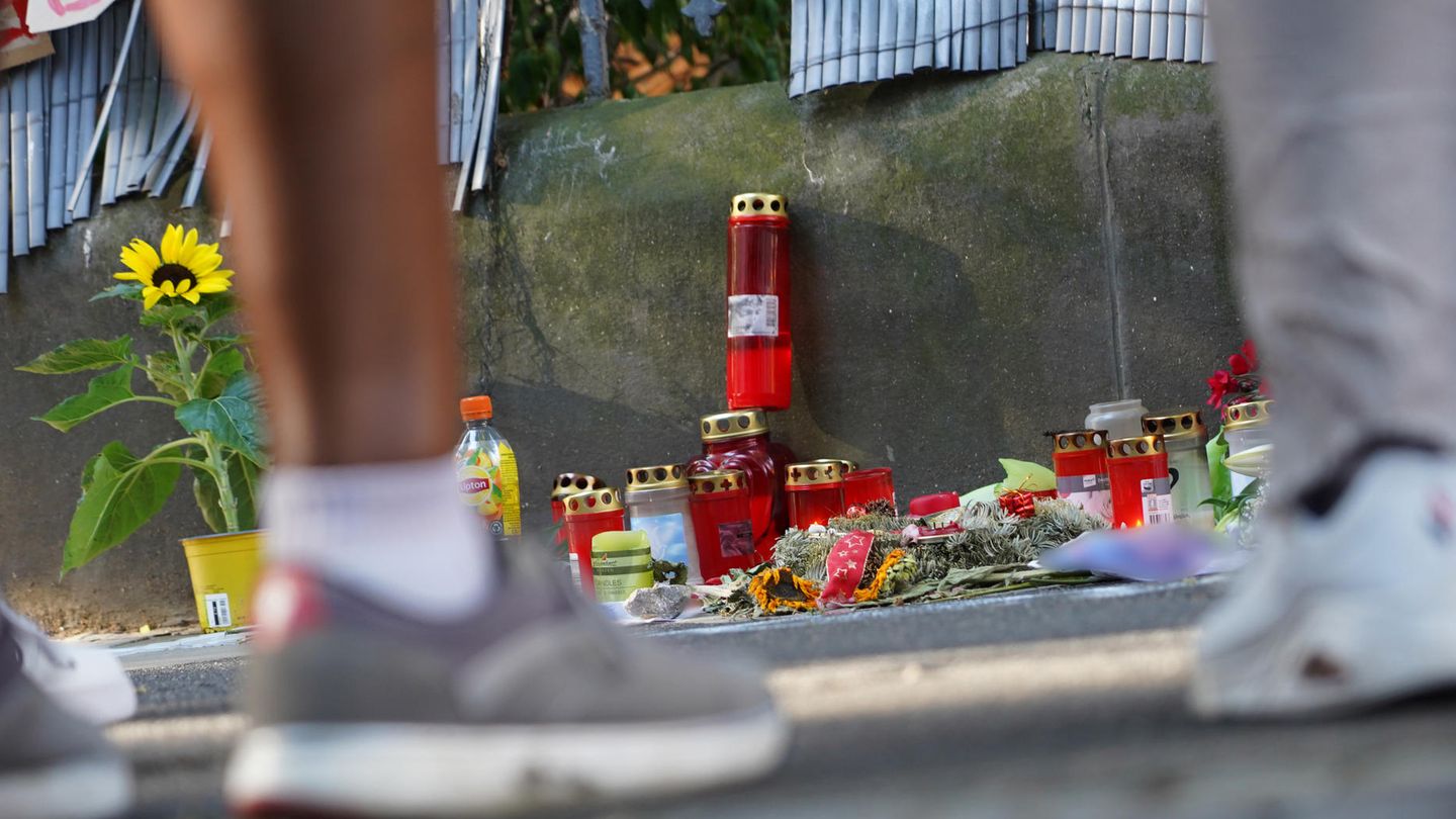 Menschen stehen vor einem Zaun, an dem mit Kerzen und Blumen eines von der Polizei erschossenen Jugendlichen gedacht wird 