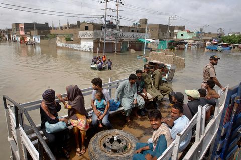 Menschen in Pakistan sitzen im überfluteten Gebiet auf der Ladefläche eines LWK