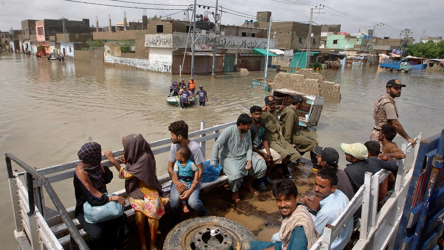 Menschen in Pakistan sitzen im überfluteten Gebiet auf der Ladefläche eines LWK