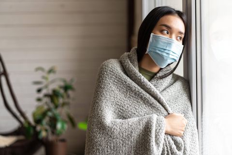 Eine Frau mit Mundschutz schaut aus dem Fenster.