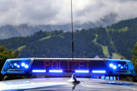 Zwischen zwei leuchtenden Blaulichtern ist in rot der Schriftzug "Polizei" zu sehen. Im Hintergrund ein Bergwald
