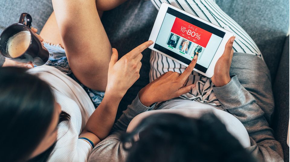 Zwei FRauen sitzen mit Tablet auf Sofa und shoppen online Schnäppchen