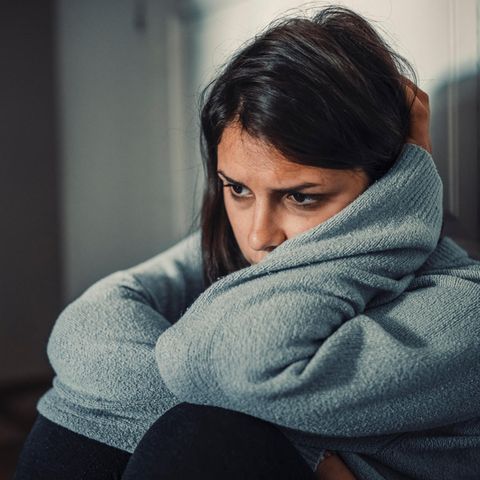 Eine Frau sitzt mit verweinten Augen auf dem Boden