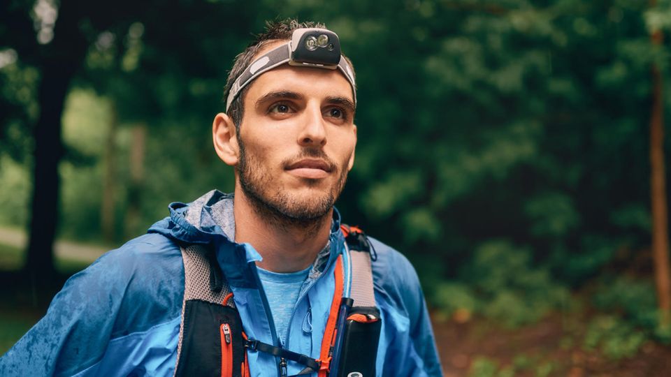 Joggen im Dunkeln: Ultra-Läufer mit Trinkrucksack und Stirnlampe im Wald