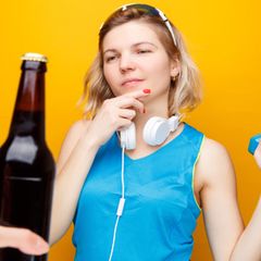 Alkohol und Laufen: Eine Sportlerin schaut auf eine Flasche Bier