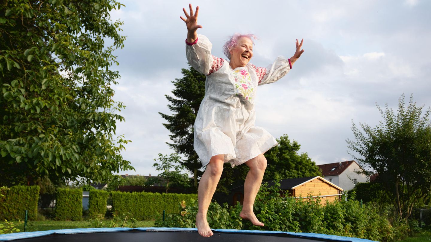 Eine ältere Frau springt glücklich auf einem Trampolin.
