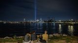 New York, USA. Menschen sitzen vor dem East River und der Installation "Tribute in Light" inmitten der Skyline von Manhattan, die an die Terroranschläge vom 11. September erinnert.