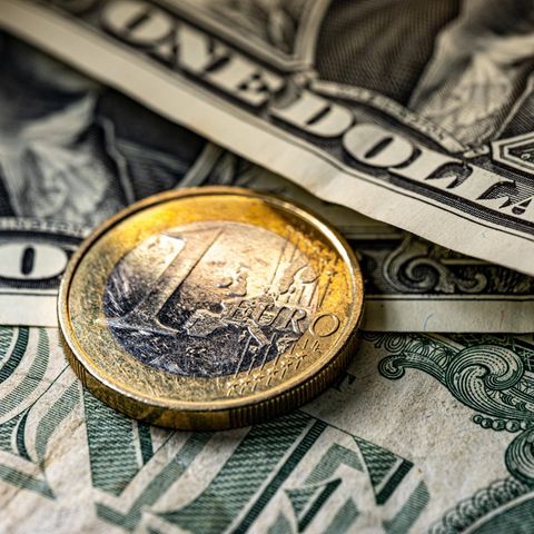 Eine Ein-Euro-Münze liegt auf mehreren Dollar-Scheinen