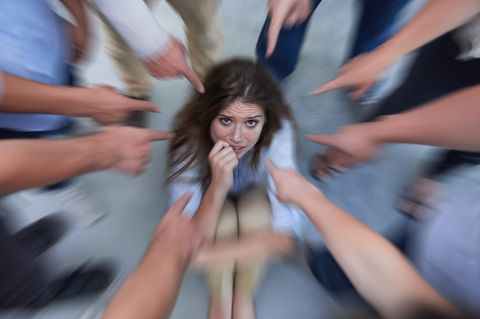 Eine Frau sitzt auf dem Boden, während viele Leute mit dem Finger auf sie zeigen.